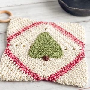 May include: A white crocheted pot holder with red stripes and a green crocheted tree design in the center.