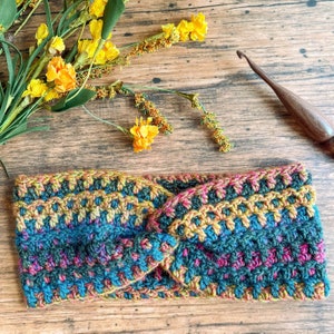 May include: A colorful crocheted headband with a twisted knot design. The headband is made with a variety of shades of blue, green, yellow, and pink yarn.
