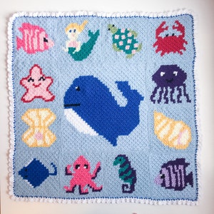 May include: A crocheted baby blanket with a blue background and various sea creatures including a whale, starfish, octopus, seahorse, and fish. The blanket is bordered with a white crocheted trim.