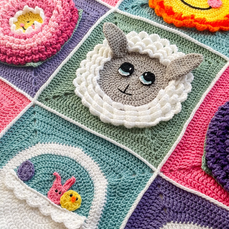 May include: A colorful crocheted baby blanket with a variety of animal and floral motifs. The blanket features a green square with a white crocheted lamb, a pink square with a purple flower, a blue square with a rainbow and two birds, and a purple square with a purple flower.