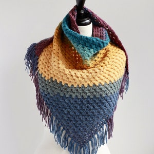 May include: A multi-colored crocheted shawl with a triangular shape and fringe. The shawl is made in shades of purple, teal, yellow, and blue.