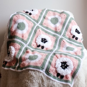May include: A crocheted baby blanket with a pink and green color scheme. The blanket features a repeating pattern of white sheep with black faces.