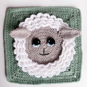 May include: A crocheted sheep square with a white fluffy fleece and a light brown face. The sheep has black eyes and a smiling mouth. The square is surrounded by a green crocheted border.