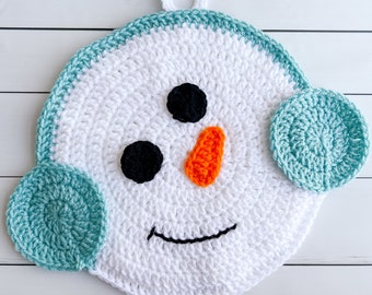 May include: A white crocheted snowman ornament with a black mouth, black eyes, and an orange nose. The snowman has two teal crocheted earmuffs.