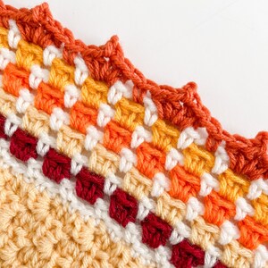 May include: A close-up of a crocheted blanket with a scalloped edge. The blanket is made with a variety of colors, including red, orange, yellow, and white.