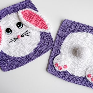 May include: Two crocheted bunny squares, one with a face and ears, the other with a tail and feet. Both squares are purple with white and pink details.