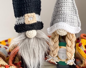 Pode incluir: Duas capas de garrafa de vinho feitas à mão em crochê. Uma é um gnomo preto e cinza com uma longa barba cinza e um chapéu alto. A outra é um gnomo cinza com tranças loiras e um chapéu pontudo. As capas são decorativas.