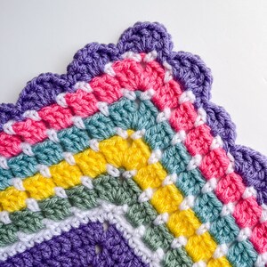 May include: A colorful crocheted blanket with a scalloped edge. The blanket is made in shades of purple, pink, green, yellow, and white.