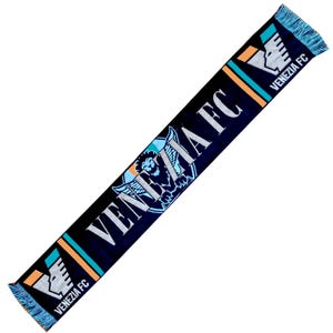 May include: A black knit scarf featuring the text VENEZIA FC in white lettering, accented with orange and teal stripes. The design includes a winged lion emblem and the VENEZIA FC logo at both ends, finished with light blue and orange fringe.