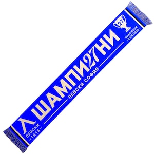 Op de afbeelding: Een blauwe sjaal met witte tekst en franjes. De sjaal heeft de tekst "ШAMПИOHИ 27" en "ЛЕВСКИ СОФИЯ", samen met een trofee-afbeelding en de jaren "2025/2026" en "1914".