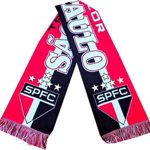 Pu&ograve; includere: Una sciarpa lavorata a maglia rossa, nera e bianca con la scritta "SAO PAULO" e "SPFC" in evidenza. La sciarpa presenta un bordo con frange e dettagli a stella, che mostrano i colori e il marchio della squadra.