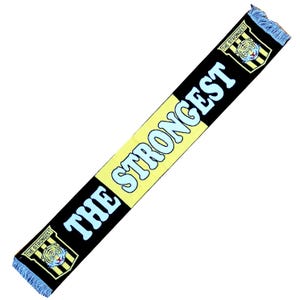 Pode incluir: Um cachecol preto, amarelo e azul com o texto "THE STRONGEST" em azul claro. O cachecol tem um emblema de tigre em cada extremidade e franjas azuis.