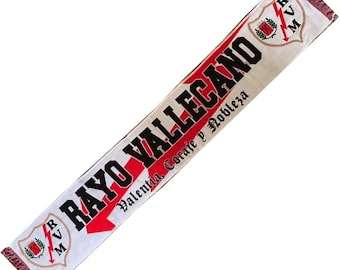 May include: White and red soccer scarf with the text "RAYO VALLECANO" and the words "Valentia, Coraje y Nobleza" in black. The scarf has a red lightning bolt and a red rose on a white shield with the letters "R.V.M."