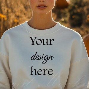 May include: A white sweatshirt with the text "Your design here" printed on the front. The sweatshirt is being modeled by a person with short brown hair in a field of tall grass.