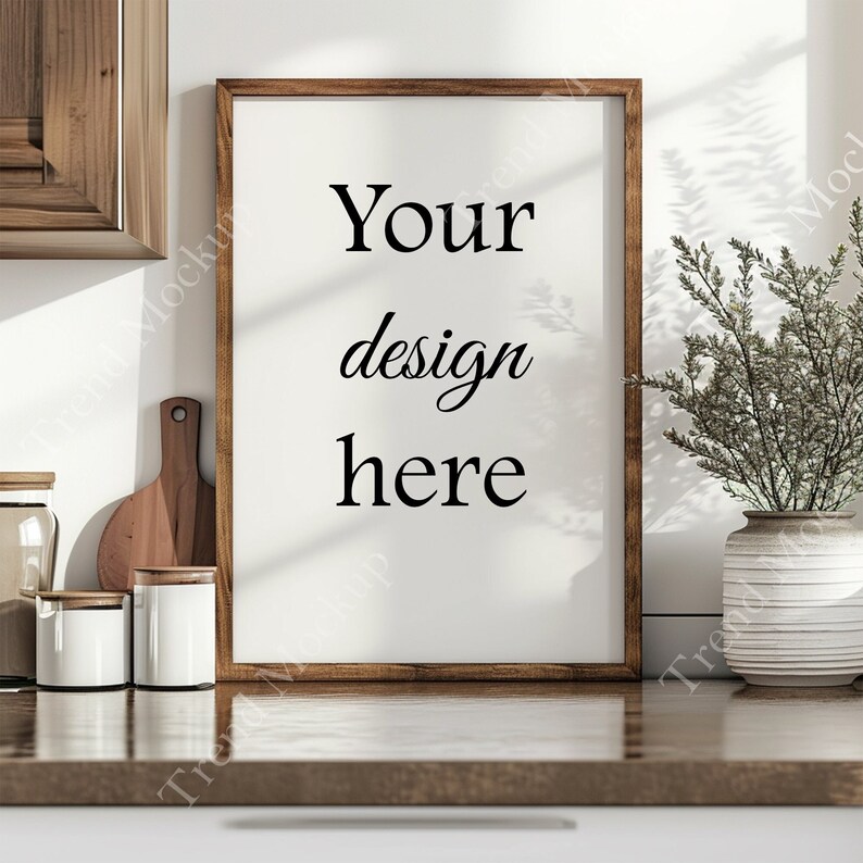 May include: A brown wooden frame with a white mat and the text "Your design here" on a white background. The frame is sitting on a wooden countertop with a vase of dried flowers and kitchen supplies.