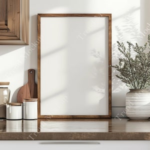 May include: A brown wooden frame with a white background sits on a wooden countertop. There are three white ceramic canisters and a wooden cutting board on the counter. A potted plant with green leaves is on the right side of the frame.