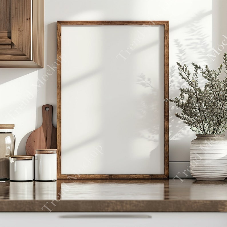 May include: A brown wooden frame with a white background sits on a wooden countertop. There are three white ceramic canisters and a wooden cutting board on the counter. A potted plant with green leaves is on the right side of the frame.