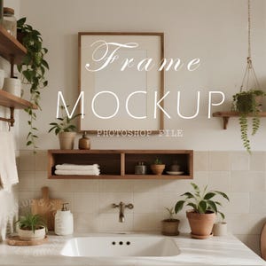 May include: A bathroom scene featuring a large, empty picture frame labeled "Frame Mockup Photoshop File." The room has a neutral color palette with wooden shelves, a sink, and potted plants. The overall aesthetic is minimalist and natural.