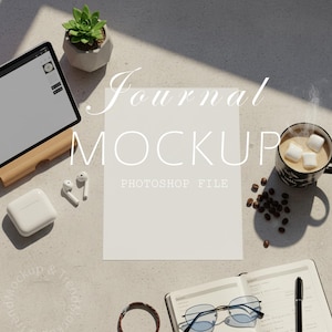 May include: A journal mockup with a blank white paper in the center, surrounded by a tablet on a wooden stand, a succulent in a concrete pot, coffee with marshmallows, and other accessories. The text "Journal Mockup" and "Photoshop File" are visible.