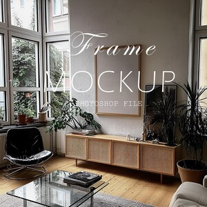 Op de afbeelding: Een lichte houten frame mockup met een witte passe-partout en een witte achtergrond. De frame staat op een lichte houten plank met een geweven rotan kast eronder. De frame bevindt zich in een woonkamer met een glazen salontafel, een zwarte stoel en planten.