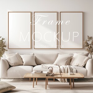 May include: Three gold picture frames with white mats hanging on a white wall above a beige sofa with pillows and a throw blanket. A wooden coffee table with books and a decorative object sits in front of the sofa.
