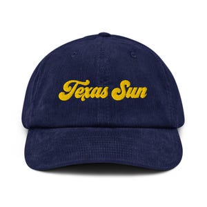 May include: A navy blue corduroy baseball cap with the text "Texas Sun" embroidered in yellow.