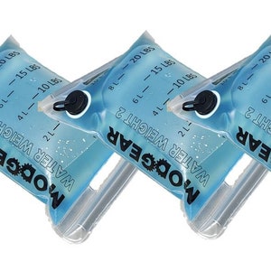 Op de afbeelding: Drie doorzichtige watergewichtzakken van plastic met blauwe vloeistof erin. De zakken hebben een zwarte dop en een handvat. De zakken zijn gemarkeerd met "MODGEAR WATER WEIGHT 2" en hebben markeringen voor 2L, 4L, 6L, 8L, 10L, 15L en 20L.