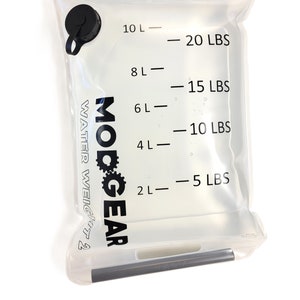 May include: A clear plastic water bladder with a black cap and a black handle. The bladder has a scale printed on it that shows the water weight in liters and pounds. The text "MODGEAR" and "WATER WEIGHT" are printed on the bladder. The text "COSMETIC DEFECT" is printed below the bladder.