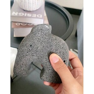 May include: A grey, textured, abstract sculpture with a rounded, organic shape. The sculpture has a hole on the side and is made of a porous material.