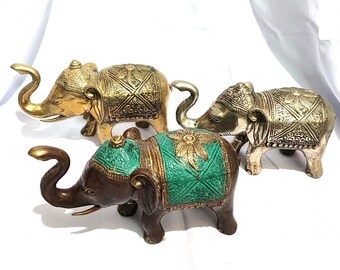 Puede incluir: Tres figuritas decorativas de elefante hechas de latón. Los elefantes son de diferentes colores: dorado, plateado y marrón. Los elefantes tienen detalles intrincados y están decorados con pintura verde y dorada.