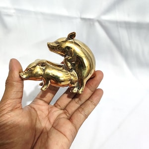 Könnte beinhalten: Eine goldfarbene Metallskulptur von zwei Schweinen in Paarungsposition.