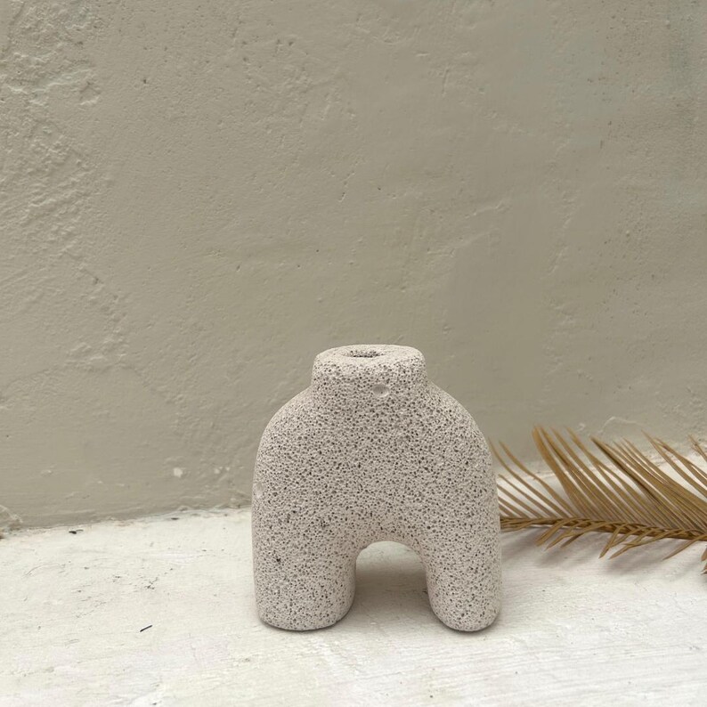 May include: A white ceramic vase with a textured surface. The vase has a unique, abstract shape with two legs.