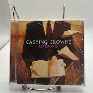 May include: A Casting Crowns Lifesong music CD in a clear plastic jewel case. The cover art features a person in a dark suit and tie holding an open book against a background of golden wheat fields. The text Casting Crowns and Lifesong is visible.