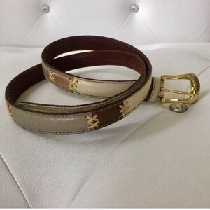 Op de afbeelding: Een bruine, beige en witte leren riem met een gouden gesp. De riem heeft een geweven ontwerp.