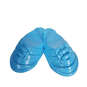 May include: A pair of light blue plastic shoe moulds, designed to resemble trainers. The moulds are connected at the heel with a central post. The shoes have textured details and simulated laces.