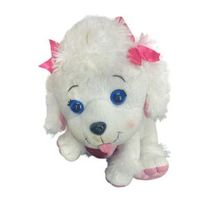 Puede incluir: Juguete de peluche de caniche blanco con lazos rosas y ojos azules. El caniche tiene la lengua rosa que sobresale.