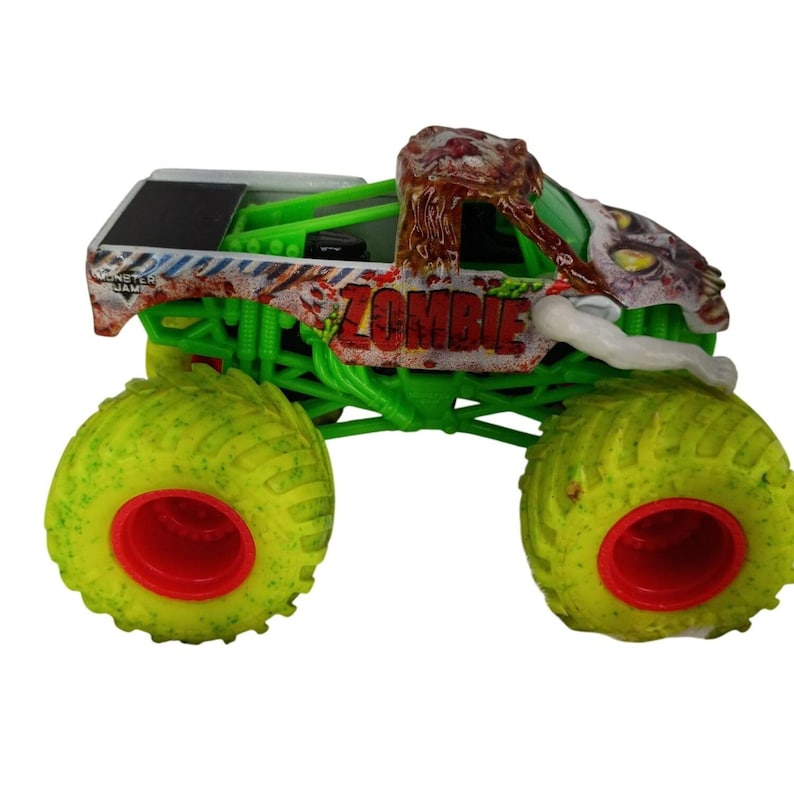 May include: A toy monster truck with a zombie theme. The truck features a green chassis, yellow tires with red rims, and a cab designed to look like a zombie head. The word "ZOMBIE" is printed on the side.