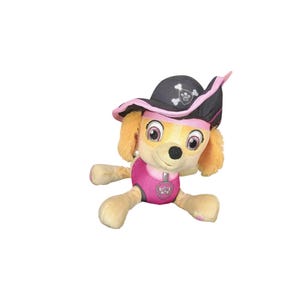 May include: A plush toy of a dog wearing a pink and black pirate hat. The dog has brown eyes, a pink nose, and a pink collar with a paw print on it.