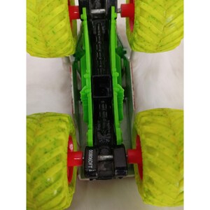 May include: A toy monster truck with large, textured, lime green tires and red wheel hubs. The truck's chassis is green and black, with a silver and red body. The text "00806DFT" is visible on the chassis.