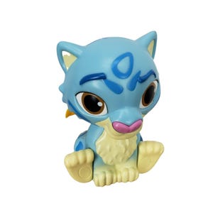 May include: A light blue cartoon figurine of a cat-like creature with large brown eyes, a pink nose, and light yellow accents. The figurine has blue markings and is sitting with its paws out.
