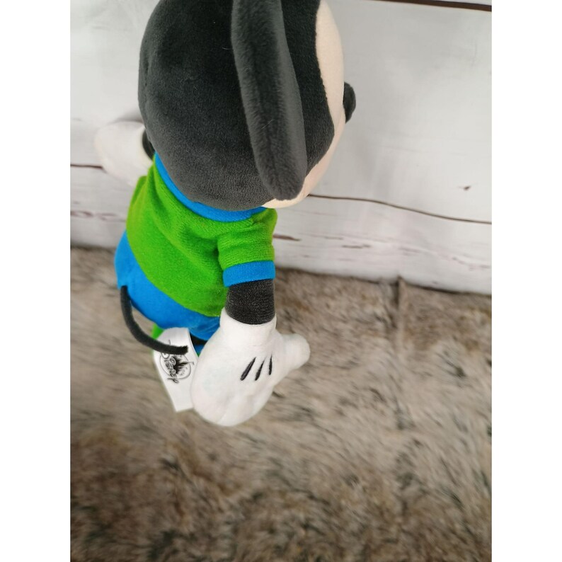 May include: A plush Mickey Mouse toy, featuring a black head and ears, a white face, and white gloves with black lines. The toy wears a green and blue striped shirt. The tail is black. The toy is a Disney collectible.