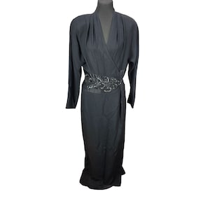 May include: A black wrap dress with long sleeves and a decorative belt. The dress has a V-neckline and a floor-length skirt. The belt is embellished with dark sequins. The dress is displayed on a black mannequin.
