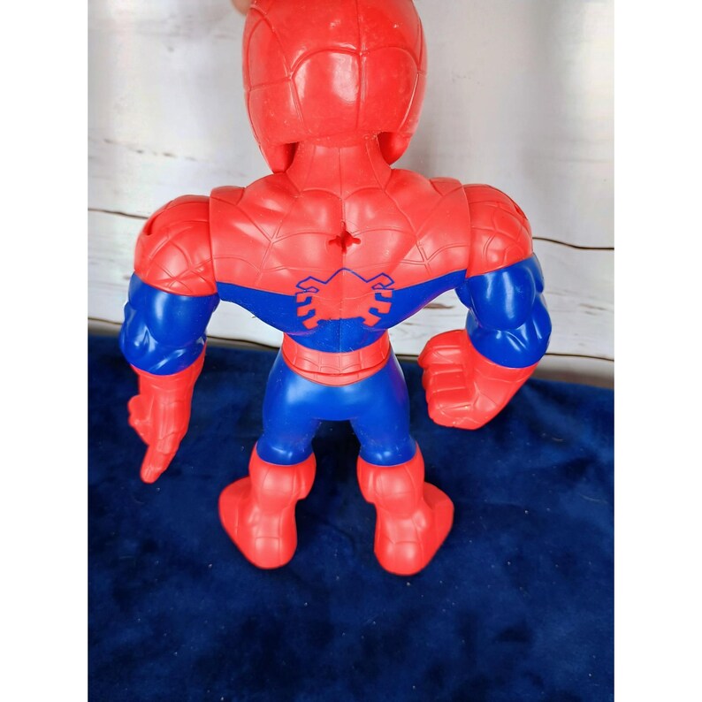 Puede incluir: Una figura de acci&oacute;n de pl&aacute;stico roja y azul de Spiderman. La figura tiene un dise&ntilde;o de telara&ntilde;a en el pecho y la espalda. La figura est&aacute; en posici&oacute;n con los brazos extendidos.