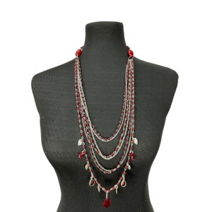 May include: A multi-strand necklace with silver chains and red teardrop-shaped beads. The necklace has several layers and features small silver charms.