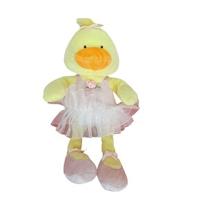 May include: A plush yellow duck wearing a pink and white tutu, ballet flats, and a matching headband. The duck has an orange beak and small black eyes. A pink rose is sewn on the bodice of the dress.