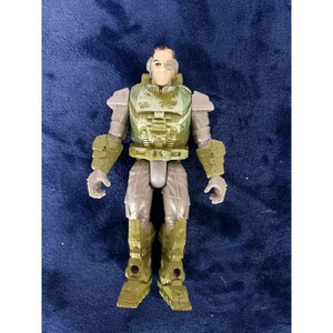Peut inclure: Une figurine d'action verte et grise d'un soldat portant un casque et une armure. La figurine a un seul œil et une expression sérieuse.