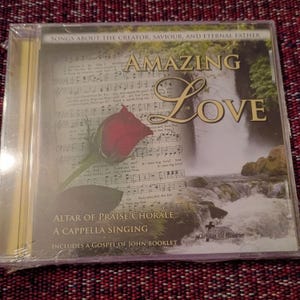Peut inclure: Un boîtier de CD avec le titre "Amazing Love" et une rose rouge sur la couverture. La couverture présente également une cascade et des notes de musique. Le texte comprend "Songs About The Creator, Saviour, And Eternal Father" et "Altar of Praise Chorale".