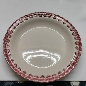 May include: Off-white ceramic pie dish with a scalloped edge. The rim is decorated with a repeating pattern of burgundy dots and shapes. The dish has a smooth, glossy surface and a deep bowl shape.