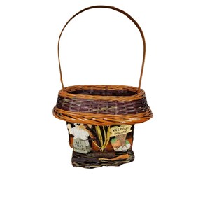 May include: A brown and purple wicker basket with a handle. The basket is decorated with Halloween-themed figures and signs that say "Keep Out Beware" and "All That Remains".