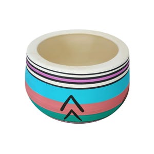 Pode incluir: Um vaso redondo de cerâmica com borda branca e interior bege. O exterior apresenta listras horizontais em turquesa, rosa, preto e roxo, com dois símbolos de seta pretos. Este vaso decorativo é adequado para plantas pequenas.